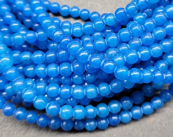 May include: A strand of light blue gemstone beads. The beads are round and smooth, and they are strung together on a clear thread. The beads are arranged in a circular pattern, and they are all the same size.