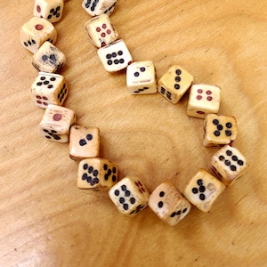 May include: A necklace made of bone dice with black and red dots. The dice are strung together with a red cord.