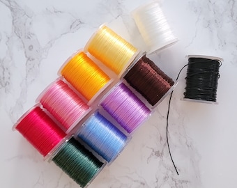 May include: Assortment of colorful spools of thread in various shades of pink, red, blue, green, yellow, purple, brown, and white. The spools are arranged in a semi-circle on a white marble surface.