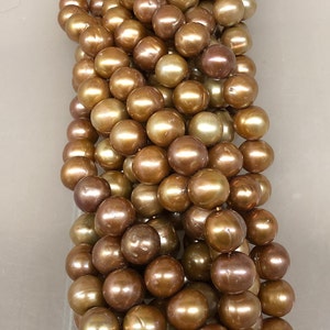 May include: A strand of golden brown pearls. The pearls are round and smooth, with a slight iridescent sheen.