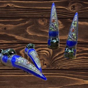 May include: Four ceramic frog figurines with blue and silver accents. The frogs are perched on top of pointed, blue and silver, ceramic horns. The horns are decorated with floral designs.