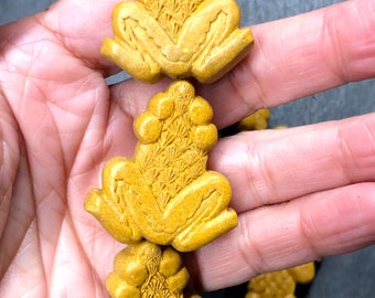 May include: A strand of yellow wooden beads, each bead is carved in the shape of a frog with a textured design on its back.