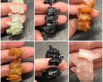 May include: A collection of carved turtle beads in various colors, including green, black, orange, and pink. The beads are strung together on a white string, showcasing the detailed craftsmanship of each turtle figurine.