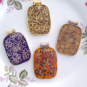 May include: Four enamel pendants with floral designs. The pendants are rectangular and have a gold-tone finish. The enamel is in shades of purple, orange, and brown.
