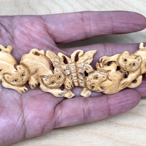 May include: A carved ivory pendant featuring five cats playing with a butterfly. The cats are intricately detailed with realistic features and are arranged in a playful, intertwined design.