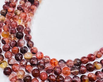 May include: A strand of round, polished beads featuring a translucent appearance with deep red, burgundy, and golden-yellow inclusions. The beads are arranged in a curved formation, showcasing varied internal patterns and natural color gradients.