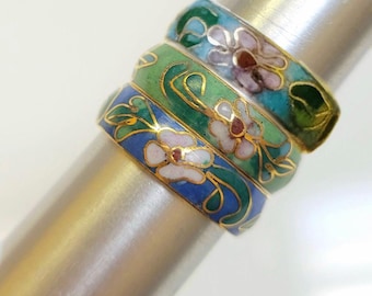 May include: Three stacked rings featuring colorful cloisonné enamel work. Each band displays a floral pattern with gold-toned metal outlines. The top ring is turquoise and green, the middle is light green, and the bottom ring is blue.