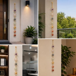 May include: A vertical wall hanging featuring seven circular gold-toned metal rings connected by a gold-toned chain. Each ring contains a different colored gemstone or crystal, arranged in a sequence of purple, clear, grey, green, yellow, orange, and red.