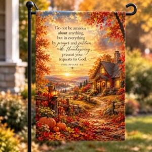 May include: A rectangular garden flag featuring an autumn landscape with a cottage, pumpkins, and fall foliage. The text reads: Do not be anxious about anything, but in everything by prayer and petition, with thanksgiving, present your requests to God. Philippians 4:6.