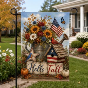 Könnte beinhalten: Eine dekorative Gartenflagge mit einer Metallgießkanne voller Sonnenblumen, Gänseblümchen und blauen Disteln. Sie enthält eine kleine amerikanische Flagge, ein Vogelhaus, einen Hüttensänger, einen Kardinal, einen Schmetterling und Kürbisse mit dem Text Hello Fall.