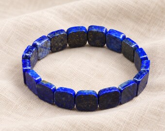 Könnte beinhalten: Ein elastisches Armband aus quadratischen Lapislazuli-Perlen. Jede Perle weist eine tiefblaue Farbe mit natürlichen goldfarbenen Pyrit-Einschlüssen auf und ist in einer durchgehenden kreisförmigen Schleife angeordnet, um das flexible Armband zu bilden.