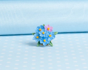 May include: A cluster of blue forget-me-not flowers with yellow centers and a single pink flower, arranged in a bouquet.