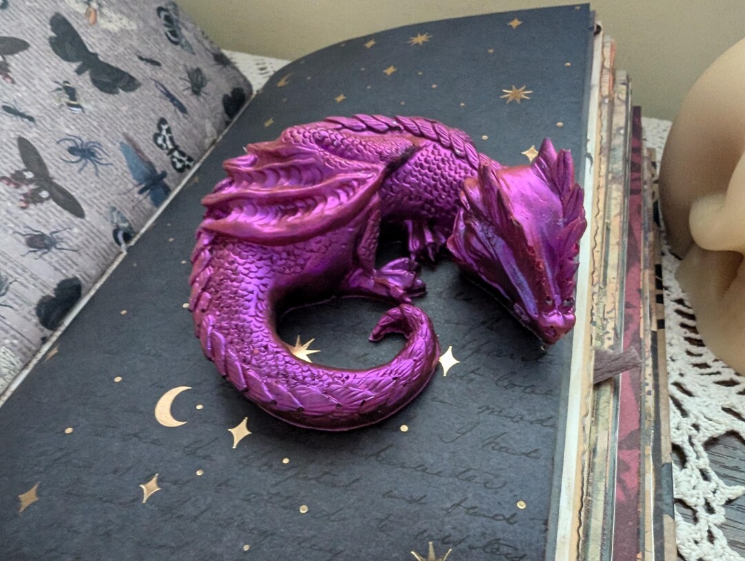 眠っているドラゴンの樹脂製の小さなフィギュア。光で明るい紫色の色が