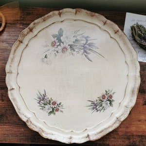 May include: A white wooden tray with a scalloped edge and a floral design. The tray has a distressed look and is perfect for serving or displaying items.