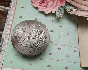 Poudre compacte en métal argenté antique par Jaciel, conçue par Norida Parfumerie, motif floral papillon en relief sur fond texturé