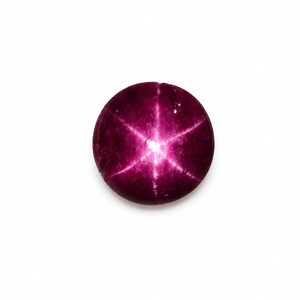 Pode incluir: Uma pedra preciosa de rubi estrela redonda de cor magenta profunda, apresentando um efeito de estrela de seis raios, conhecido como asterismo, centrado na sua superfície de cabochão lisa e polida. A gema exibe uma cor rica e saturada.