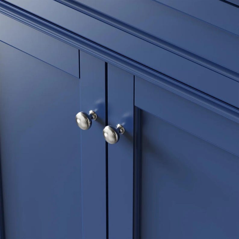 May include: A deep blue cabinet featuring two doors with recessed panels and horizontal molding at the top. Two polished silver, round, mushroom-shaped knobs are attached to the center of the doors, providing a metallic contrast to the blue finish.