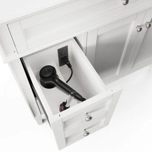 May include: A white bathroom vanity cabinet featuring an open top drawer with a built-in electrical outlet. A black hair dryer is plugged into the outlet and rests inside the drawer, which also includes a second closed drawer below it.