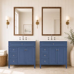 May include: Two blue bathroom vanities with white countertops, each featuring a single drawer above two cabinet doors and three side drawers. Each vanity is paired with a rectangular mirror in a brown wood frame and a wall-mounted light fixture.