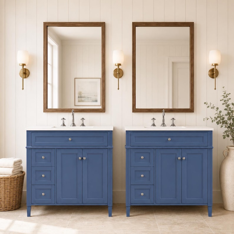 May include: Two blue bathroom vanities with white countertops, each featuring a single drawer above two cabinet doors and three side drawers. Each vanity is paired with a rectangular mirror in a brown wood frame and a wall-mounted light fixture.