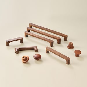 May include: A collection of dark brown wooden cabinet hardware, including four rectangular bar pulls of varying lengths and three round knobs. Each piece features a smooth, natural wood grain finish with visible screw holes for mounting.