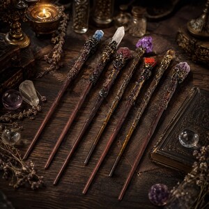 May include: A collection of six handcrafted wands featuring dark, textured wooden shafts and ornate metallic accents at the handles. Each wand is topped with a unique raw crystal point, including blue, clear, pink, purple, red, and light purple stones.