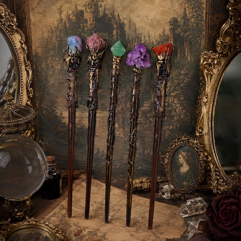 May include: Five wands with dark brown, textured handles and metallic gold accents. Each wand is topped with a unique crystal: a blue stone, a pink stone, a green stone, a cluster of purple amethyst, and a single orange stone, all held by metal claws.
