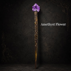 May include: A long, slender wand featuring a dark brown, textured handle wrapped in gold-colored vines. The top is adorned with a cluster of purple amethyst crystals arranged in a floral shape. The text Amethyst Flower is visible.