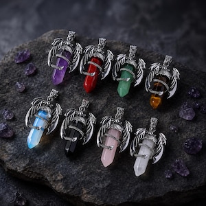 May include: Eight crystal point pendants, each featuring a silver-toned metal setting shaped like dragon wings wrapping around the stone. The collection includes purple, red, green, brown, blue, black, pink, and white translucent or opaque crystals.
