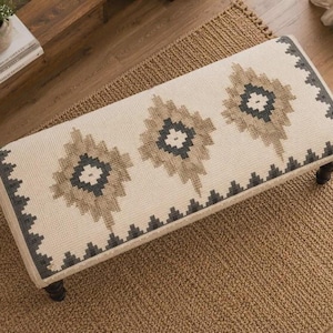 May include: A rectangular upholstered bench featuring a cream-colored fabric top with a repeating geometric diamond pattern in shades of tan and dark gray. The bench is supported by four dark brown wooden legs and has a textured, woven appearance.