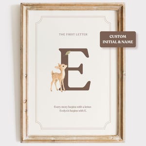 Könnte beinhalten: Ein gerahmter Wanddruck mit einem großen braunen Buchstaben E, einer kleinen Reh-Illustration und dem Text THE FIRST LETTER, Every story begins with a letter und Evelyn's begins with E. Ein braunes Etikett zeigt CUSTOM INITIAL & NAME.