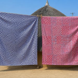 May include: Two large rectangular fabric pieces hanging on a clothesline. The left piece is dark blue with a repeating white circular pattern. The right piece is a patchwork of red and pink squares featuring intricate floral and geometric motifs.
