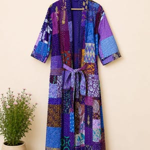 May include: A long-sleeved robe featuring a patchwork design in various shades of purple and blue. The garment is constructed from multiple fabric panels with diverse patterns, including floral and geometric motifs, and includes a matching tie belt.