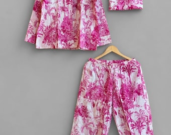 May include: A pajama set consisting of a long-sleeved button-down shirt and matching trousers, accompanied by a folded fabric pouch. The garments feature a white base with a vibrant magenta pink toile-style print depicting tropical palm trees.