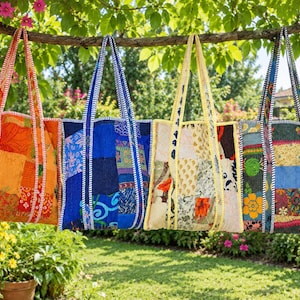 May include: Four rectangular tote bags made from patchwork fabric are hanging from a tree branch. Each bag features a unique combination of colourful patterned textile squares, two long shoulder straps, and visible white stitching along the edges.
