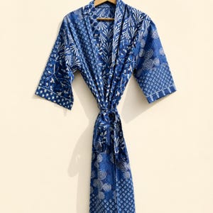 May include: A long-sleeved robe featuring a patchwork design of various blue and white geometric patterns, including circles, floral motifs, and fan shapes. The garment has a wrap-front style with a matching fabric tie belt at the waist.