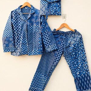 May include: A long-sleeved button-down shirt, matching pyjama trousers, and a square pouch, all featuring a patchwork design of various blue and white geometric, floral, and polka dot patterns. Each item is displayed on a wooden clothes hanger.