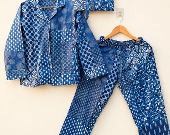 May include: A long-sleeved button-down shirt, matching pajama pants, and a square pouch, all featuring a patchwork design of various blue and white geometric, floral, and polka dot patterns. Each item is displayed on a wooden clothes hanger.