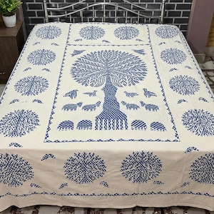 Op de afbeelding: Een crèmekleurige sprei met een herhalend patroon van donkerblauwe cirkelvormige boommotieven. Het centrale paneel toont een grote boom met een gestructureerde stam, omringd door kleine dierenfiguren, allemaal in een donkerblauwe print.