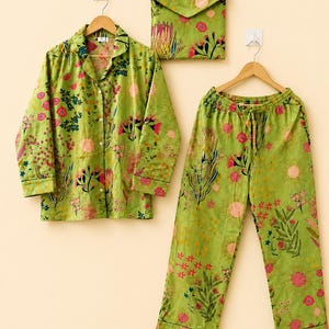 May include: A lime green pajama set featuring a long-sleeved button-down shirt and matching drawstring pants. The fabric is decorated with a colorful botanical print of pink, red, and yellow flowers, green leaves, and circular sun-like shapes.