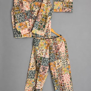 May include: A long-sleeve button-down shirt and matching trousers set featuring a multi-colored patchwork floral print in shades of orange, green, blue, and pink. The set includes a separate folded square piece of the same patterned fabric.
