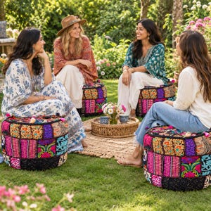 Peut inclure: Un pouf de sol rond et bas présentant un motif patchwork composé de tissus brodés aux couleurs vives, de motifs floraux complexes et de petits pompons décoratifs sur le bord supérieur, posé sur une pelouse verte dans un jardin.