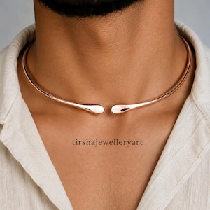 Könnte beinhalten: Ein Halsreif aus roségoldfarbenem Metall mit glattem, offenem Design und zwei abgerundeten, spitz zulaufenden Enden. Das Schmuckstück liegt um den Hals, und der Text 'tirshajewelleryart' ist mittig unter dem Halsreif zu sehen.