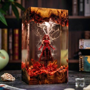May include: A rectangular resin lamp featuring a miniature Scarlet Witch figure in a red costume standing amidst red crystal-like structures. The base and top are made of natural wood with a clear resin center containing wispy white smoke effects.