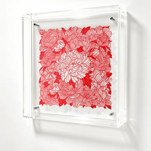 May include: A square wall art piece featuring a dense, intricate pattern of red and white line-drawn flowers. The artwork is encased in a clear, transparent acrylic box frame with four silver-toned metal mounting bolts at the corners.