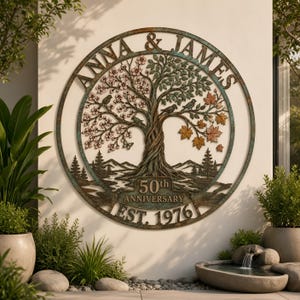 Puede incluir: Una pieza de arte mural circular de metal que muestra un árbol con follaje estacional, pájaros y mariposas. El texto dice ANNA & JAMES, 50th ANNIVERSARY y EST. 1976. El diseño incluye siluetas de montañas y pinos con un acabado de bronce envejecido.