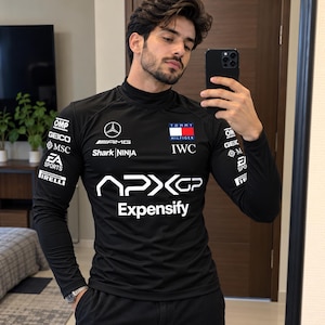 May include: A black long-sleeve mock neck shirt featuring various sponsor logos including Mercedes-AMG, Tommy Hilfiger, IWC, Shark Ninja, OMP, GEICO, MSC, EA Sports, Pirelli, APX GP, and Expensify printed in white across the chest and sleeves.