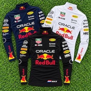 Puede incluir: Tres camisas de manga larga con cuello alto en azul marino, blanco y negro. Cada camisa presenta logotipos de Red Bull, Oracle, Tag Heuer, Mobil 1 y varios patrocinadores en el pecho y las mangas. La camisa negra incluye una pequeña bandera holandesa y el texto MAX.