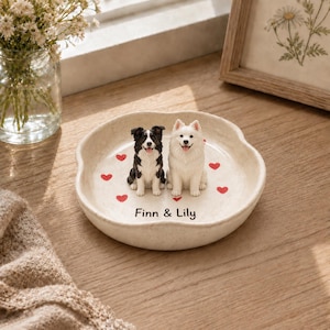 May include: A round, off-white ceramic trinket dish featuring two sculpted dog figurines, one black and white and one white, surrounded by small red heart icons. The text Finn & Lily is printed in black on the center of the dish base.