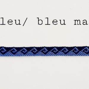 May include: A blue friendship bracelet featuring a wave pattern in shades of blue. The bracelet is made of woven threads and has an adjustable design. The text "bleu/ bleu marine" is above the bracelet.
